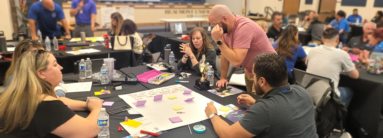 District staff around a board room table talking through a poster of sticky notes